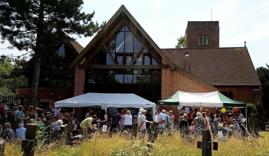 Church with a thatched roof hosting an outdoor event with tents, people, and a field in the foreground.