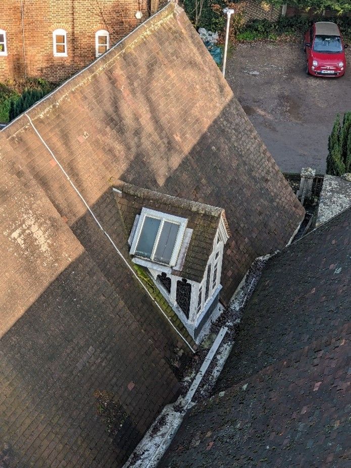 Overhead view of a tiled roof with a small dormer window, set against a backdrop of a building and a red car.