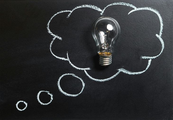 Lightbulb inside chalk-drawn thought bubble on a chalkboard.