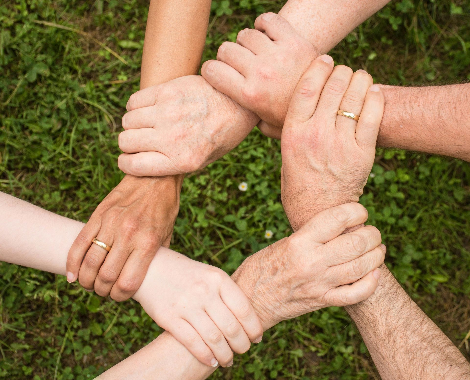 Hands clasped together in a circle, on green grass, symbolizing unity.
