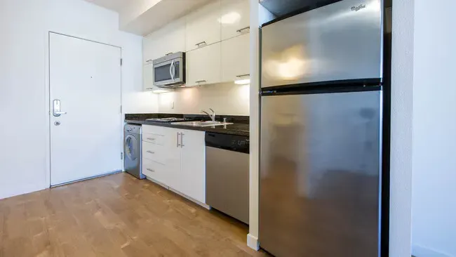 Small kitchen with stainless steel refrigerator, white cabinets, and wood flooring.