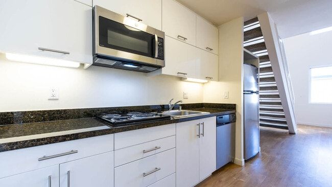 White kitchen with stainless steel appliances and dark countertop. Stairs leading up.