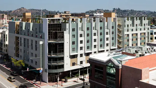 Modern, multi-story apartment building with a variety of colors on a city street, sunny day.