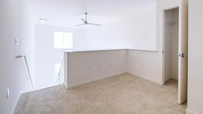 Empty loft with beige carpet, white walls, closet, and a ceiling fan.