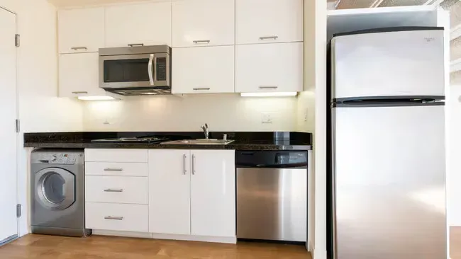 Small, modern kitchen with white cabinets, stainless steel appliances, and dark countertop.