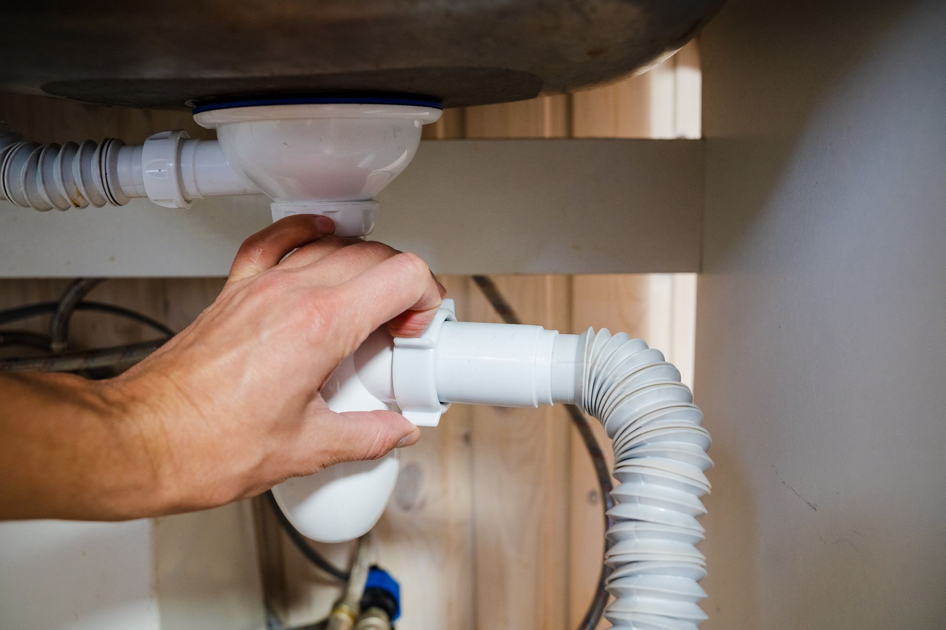 A person's hand tightening a white plastic slip nut on a sink drain pipe assembly beneath a basin.