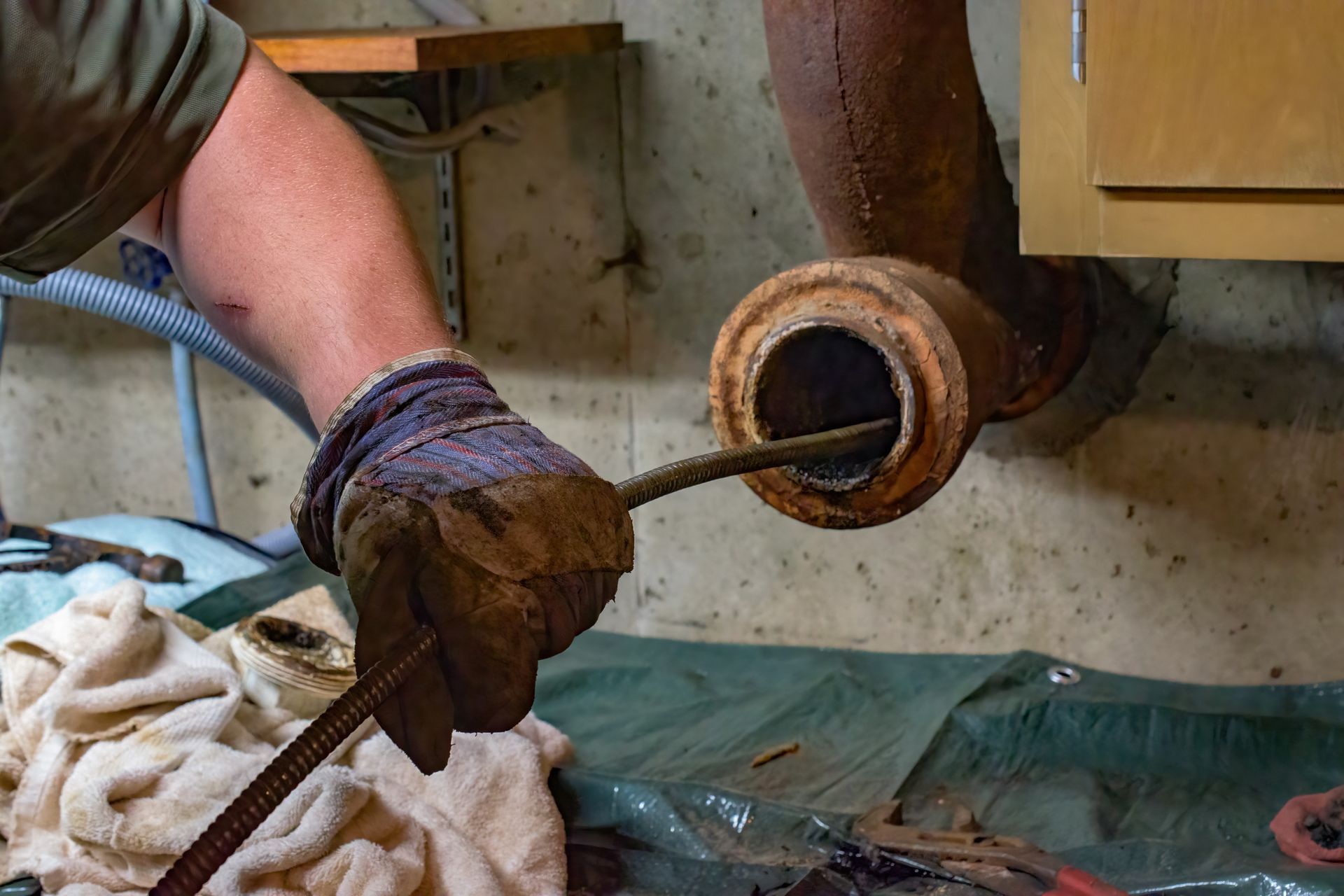 Gloved hands pulling a rusted pipe from a wall near a workbench in a workshop