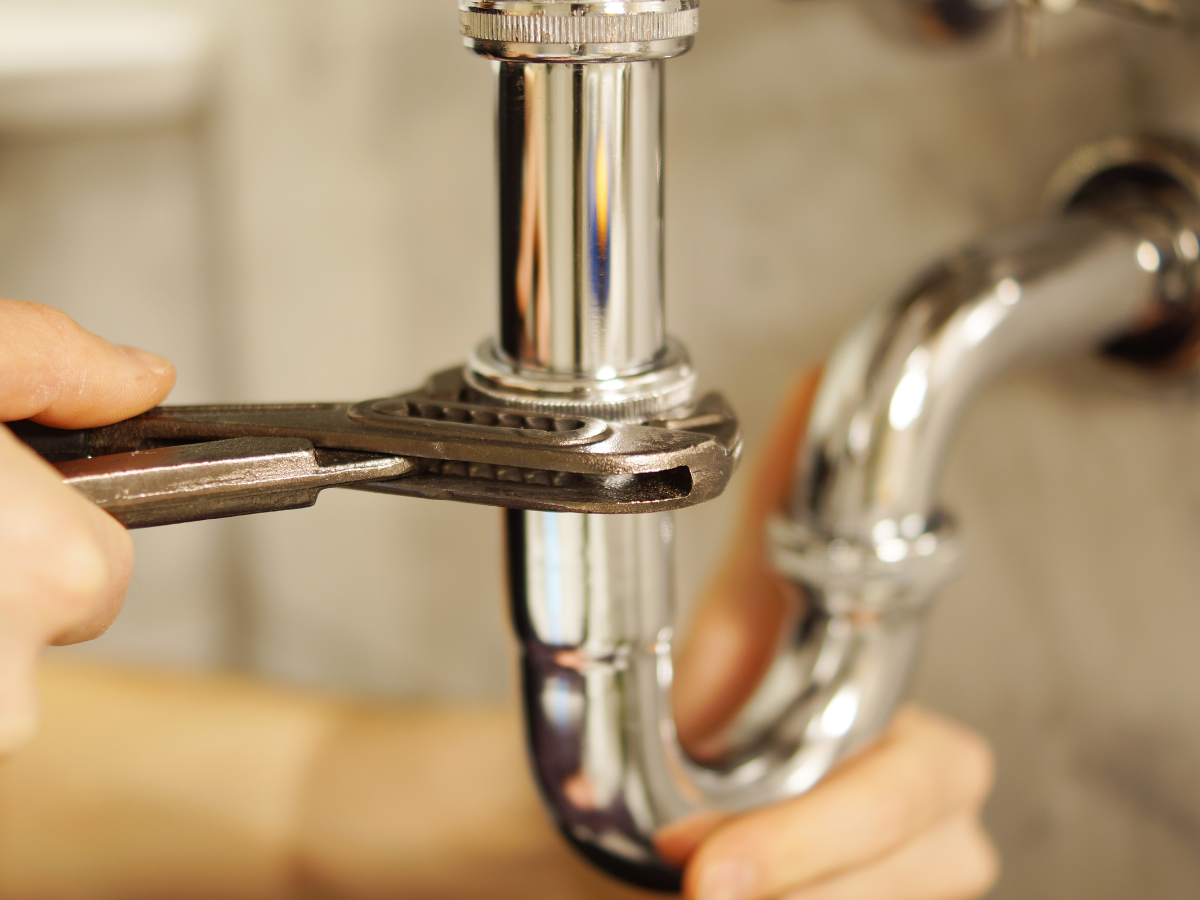 Person using a wrench to tighten a chrome pipe under a sink.