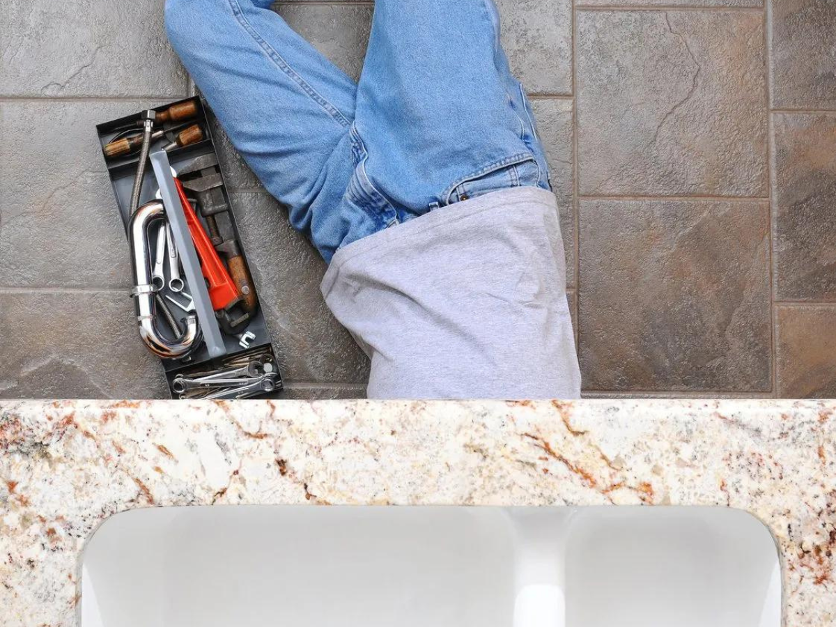 A plumber is laying on the floor next to a sink.