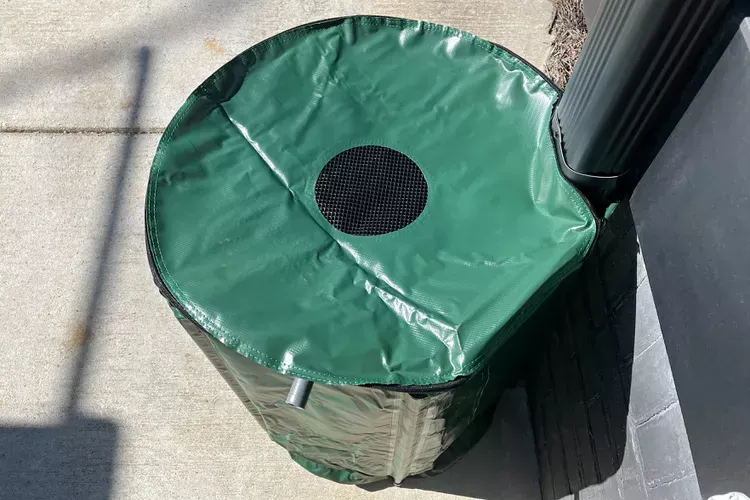 A green trash can with a hole in the middle is sitting on the sidewalk.