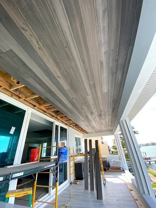 Wooden plank ceiling installation on a white building exterior with balcony and large windows; construction site.