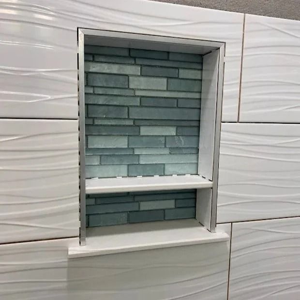 Tile shower niche with gray and blue stacked stone background. White shelf and edging.