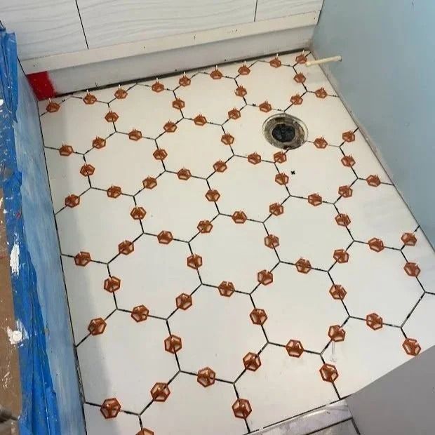 Tiled shower floor with honeycomb pattern in white, brown, and black, featuring drain and red waterproofing.