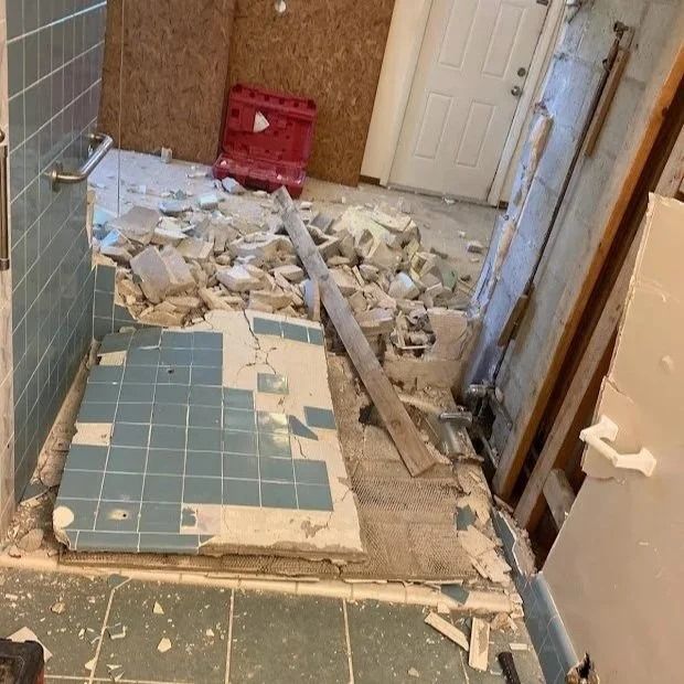 Bathroom under demolition, blue tiles, debris scattered, door and plywood visible.