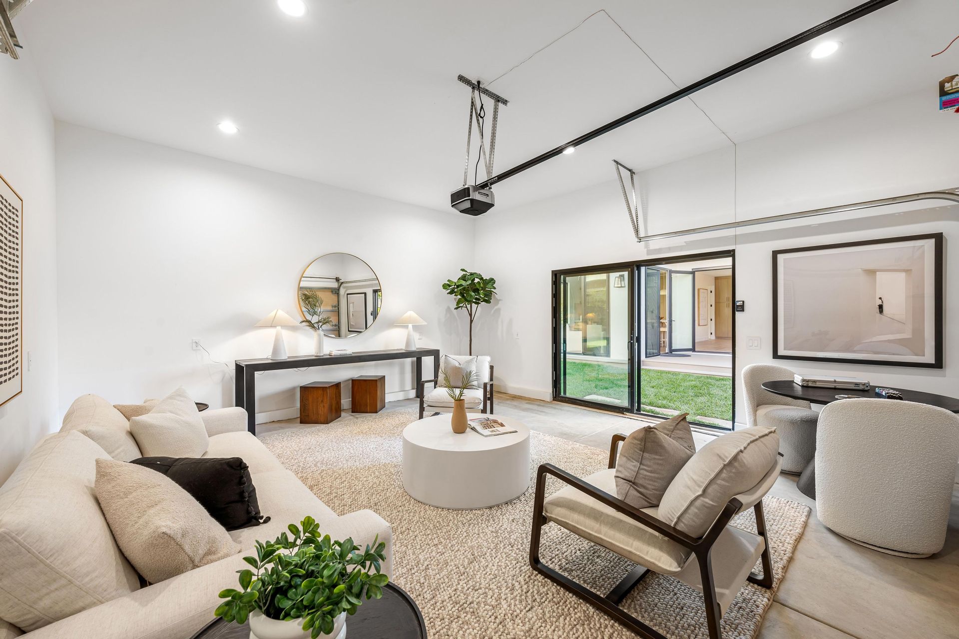 Modern living room with white walls, seating, and access to a backyard.