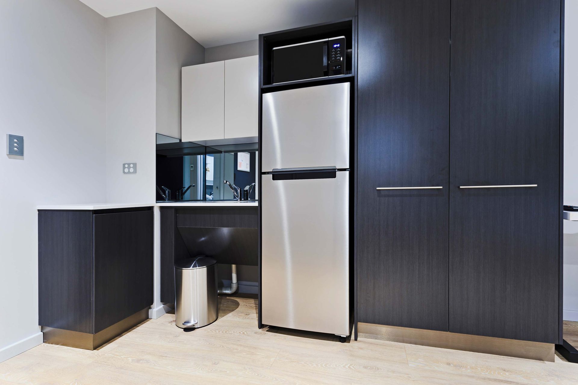 Small kitchen with stainless steel fridge, microwave, and dark gray cabinets.