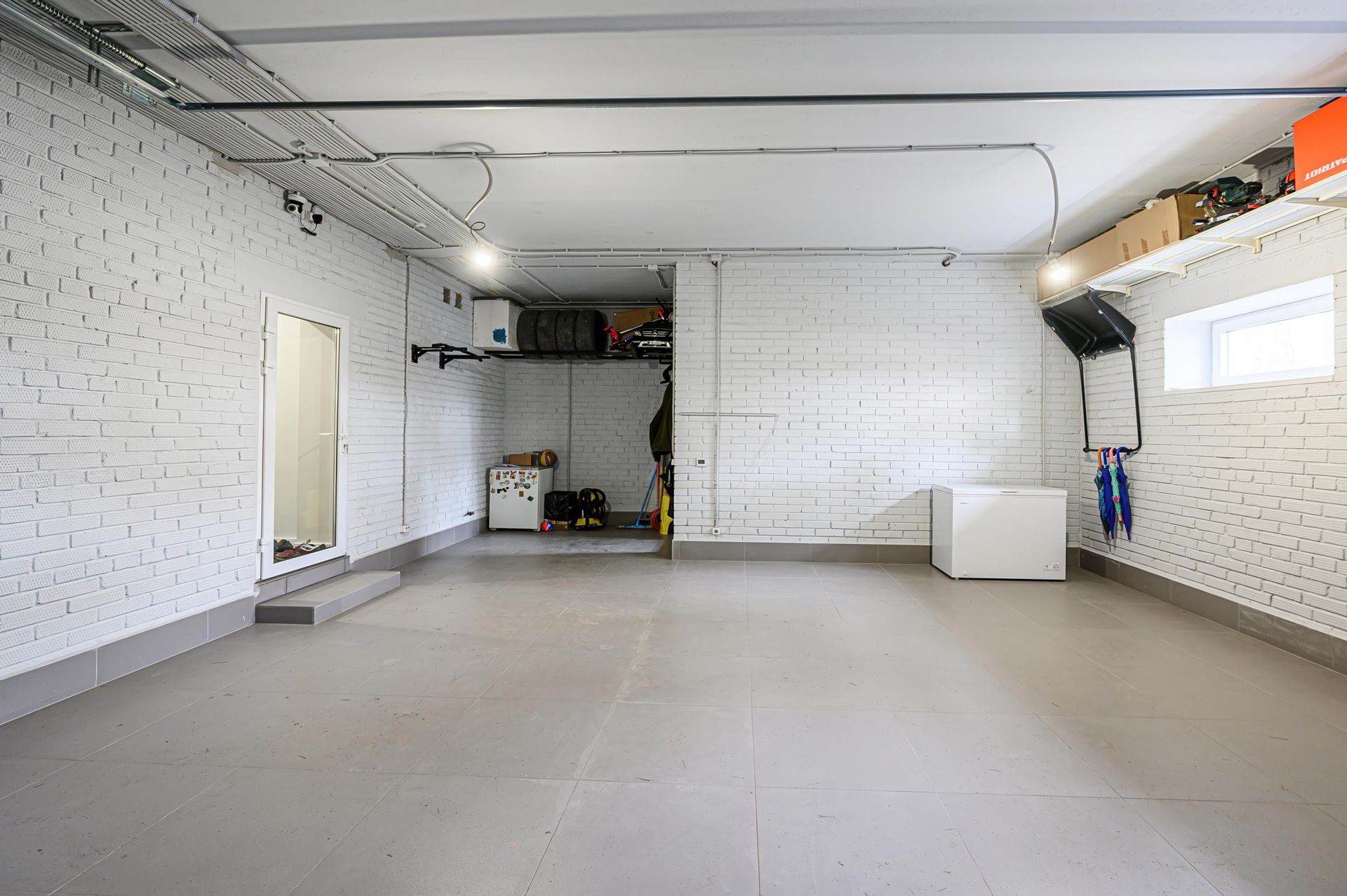 Empty garage with white brick walls, gray floor, and overhead electrical wiring.