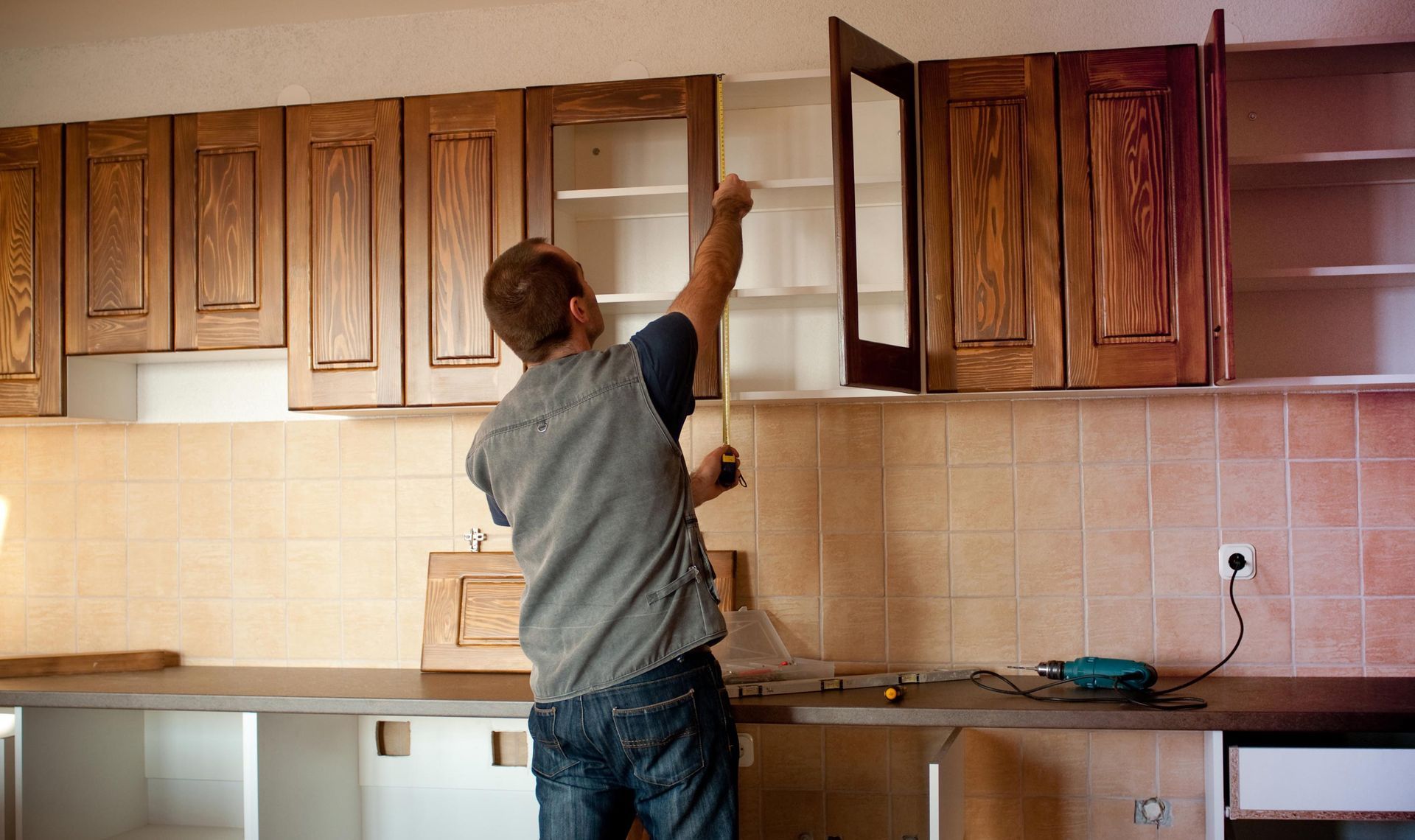 Man measuring inside kitchen cabinet during renovation.