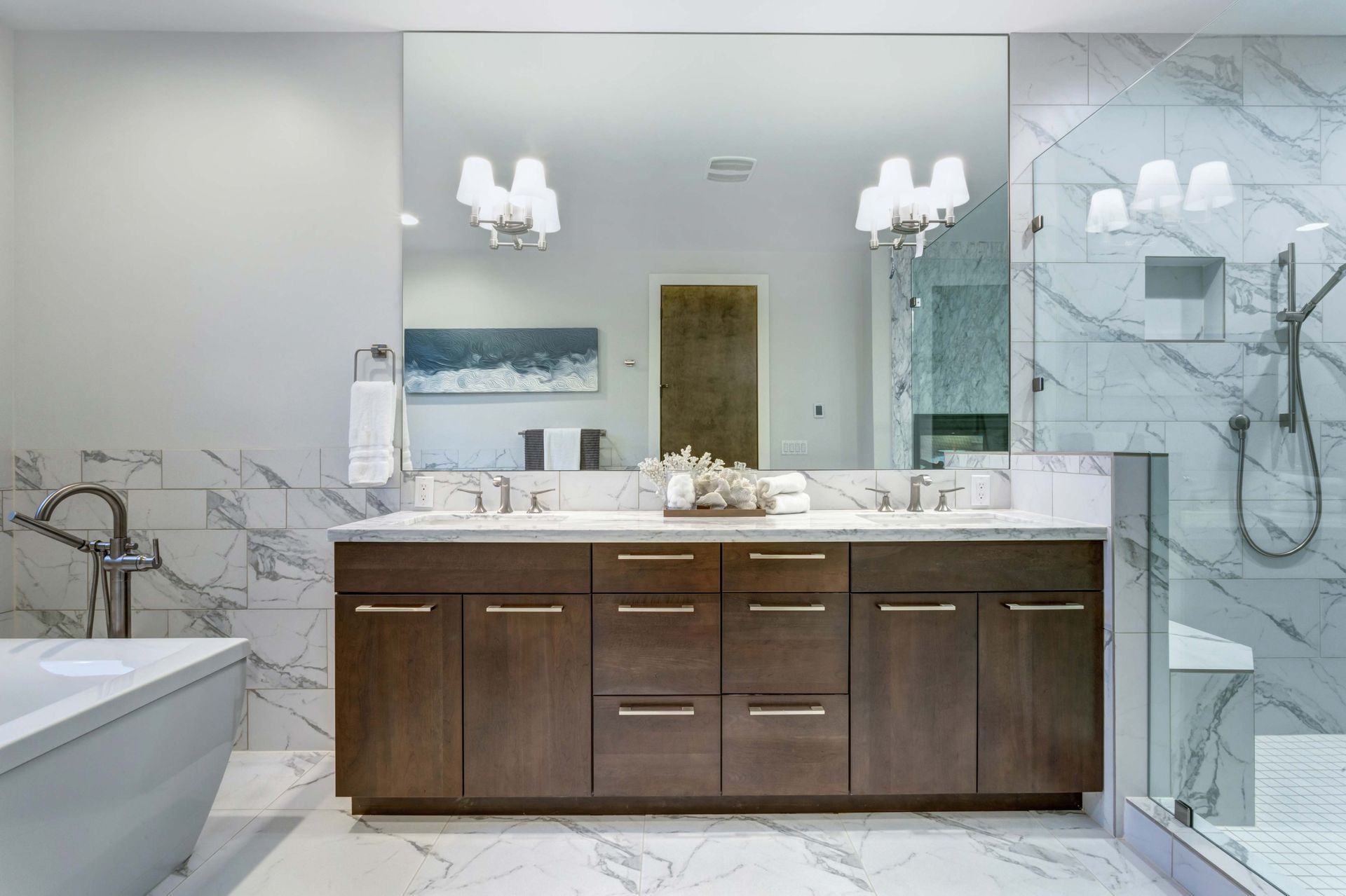 Modern bathroom with marble tile, dark wood vanity, large mirror, and glass shower.