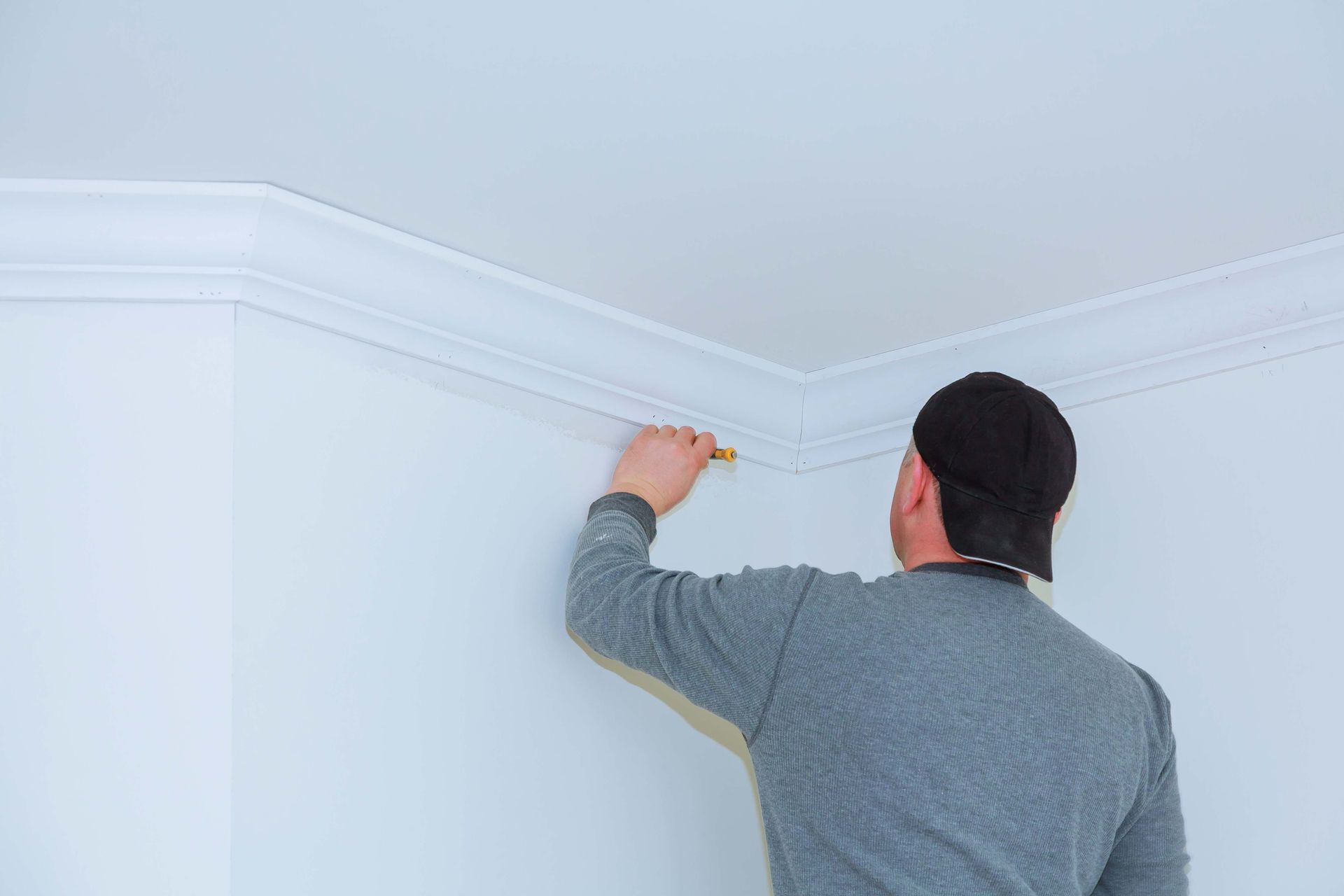 Person installing white crown molding on a white ceiling and wall.