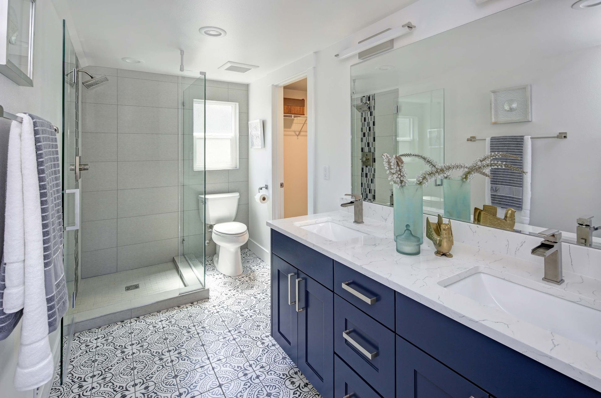 Modern bathroom with blue vanity, double sinks, glass shower, and patterned floor.