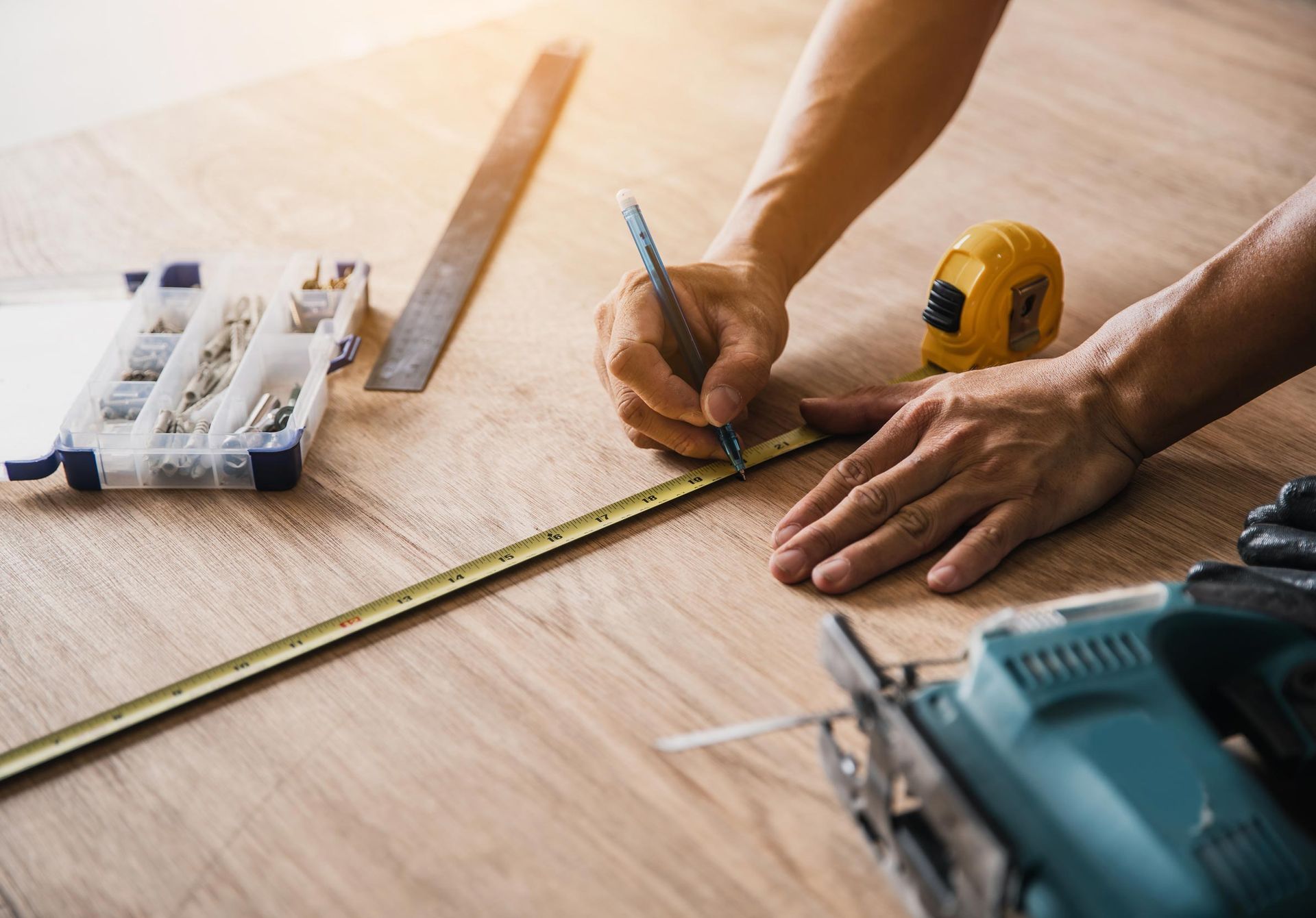Person measuring and marking wood with tools including a tape measure, pencil, and saw.