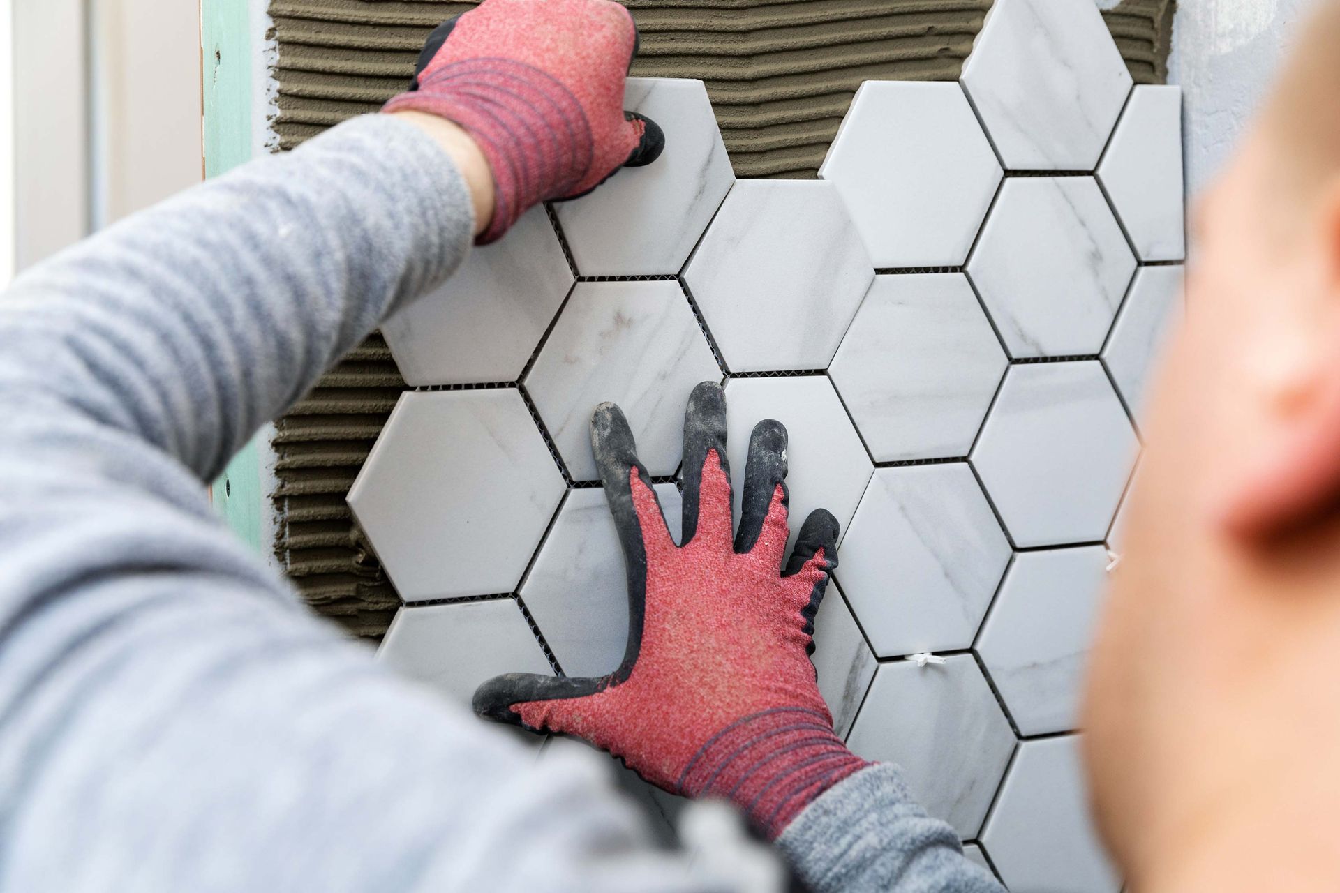 Person installing hexagonal marble tiles on a wall, wearing red gloves, close-up.