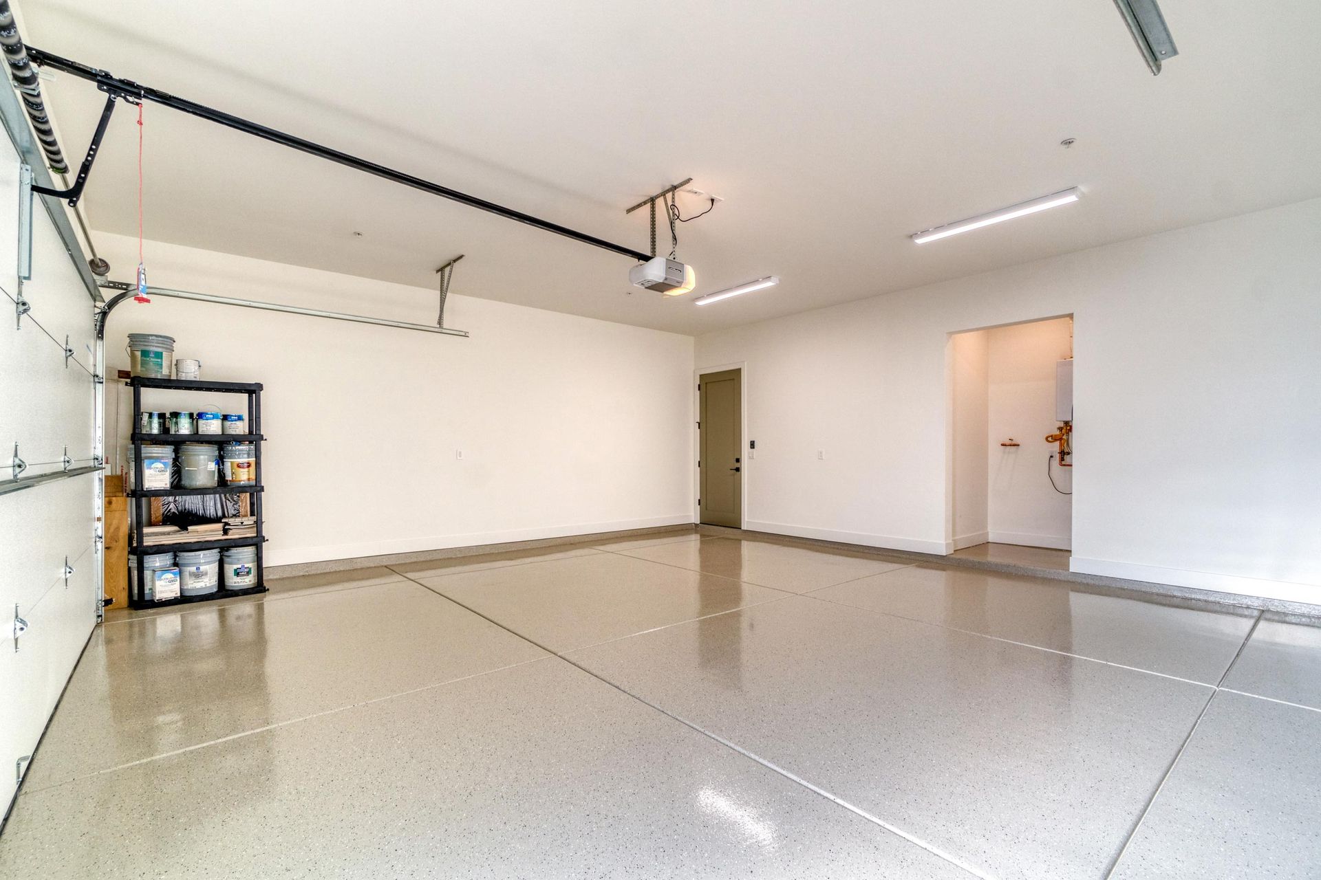 Empty, spacious garage with epoxy flooring, white walls, and a storage rack.
