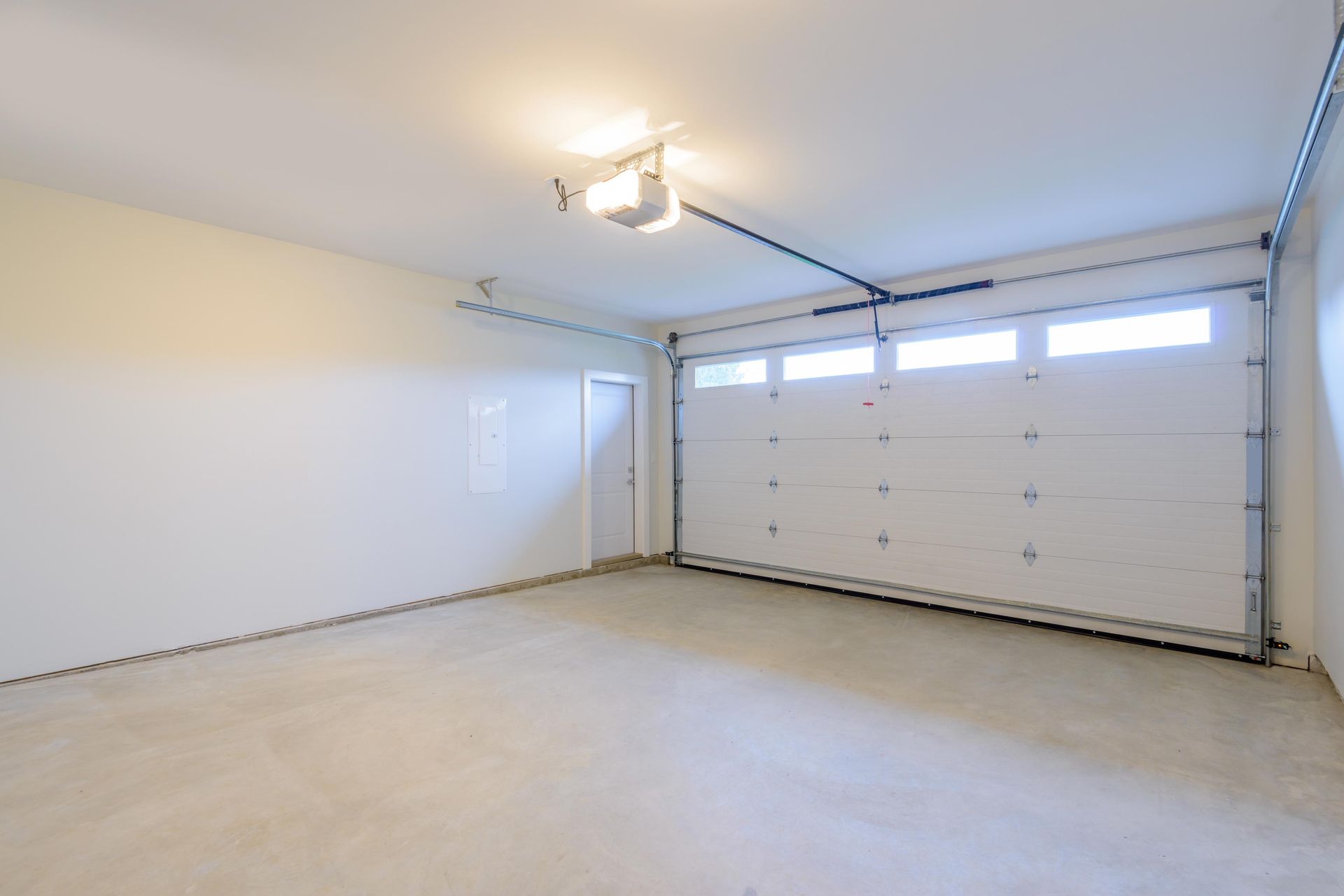 Empty, white garage with a closed overhead door and a small side door. Concrete floor.