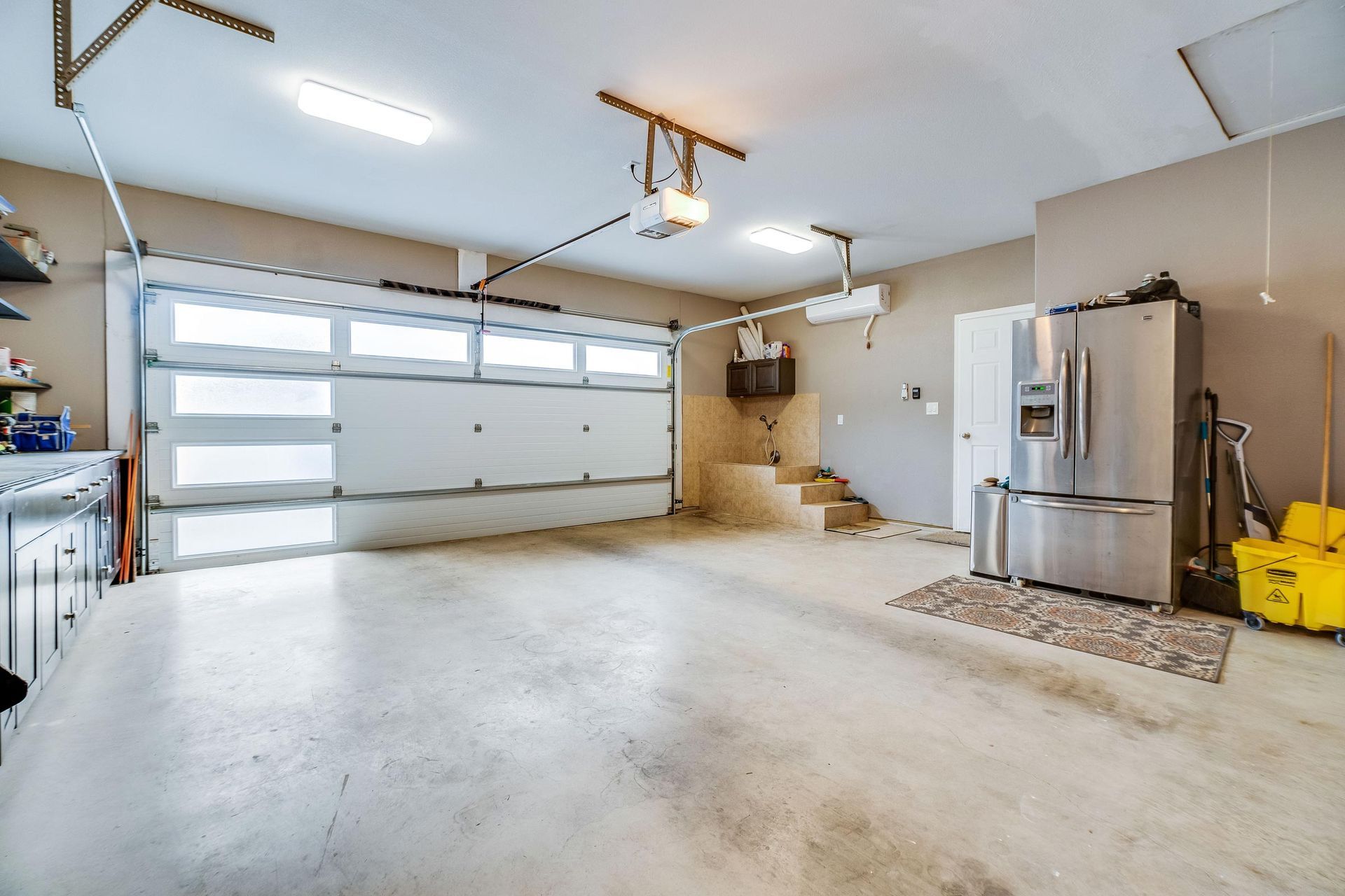 Empty garage interior with a closed white garage door, concrete floor, and a refrigerator.
