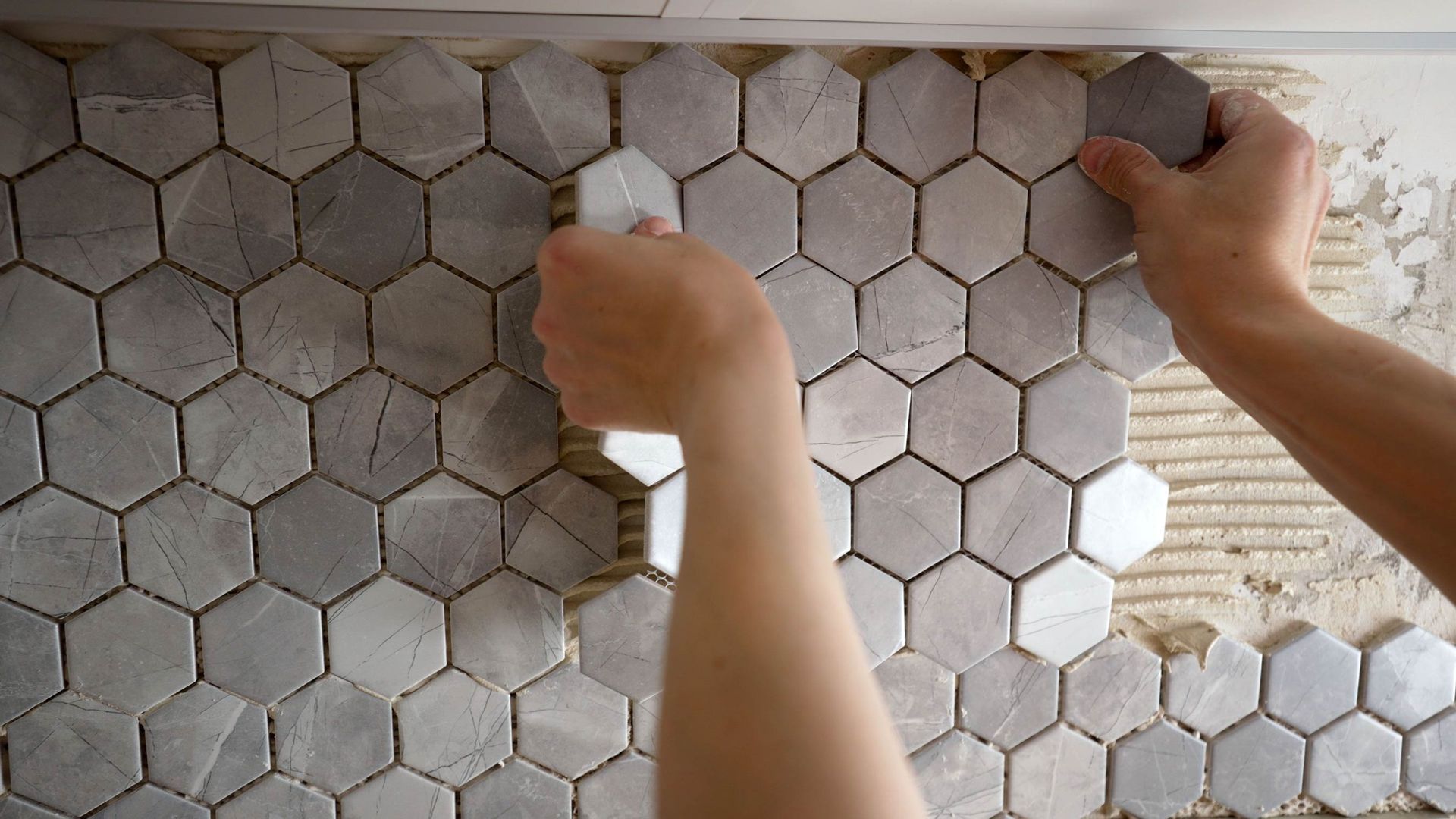 Hands placing hexagonal marble tiles on a wall during installation.