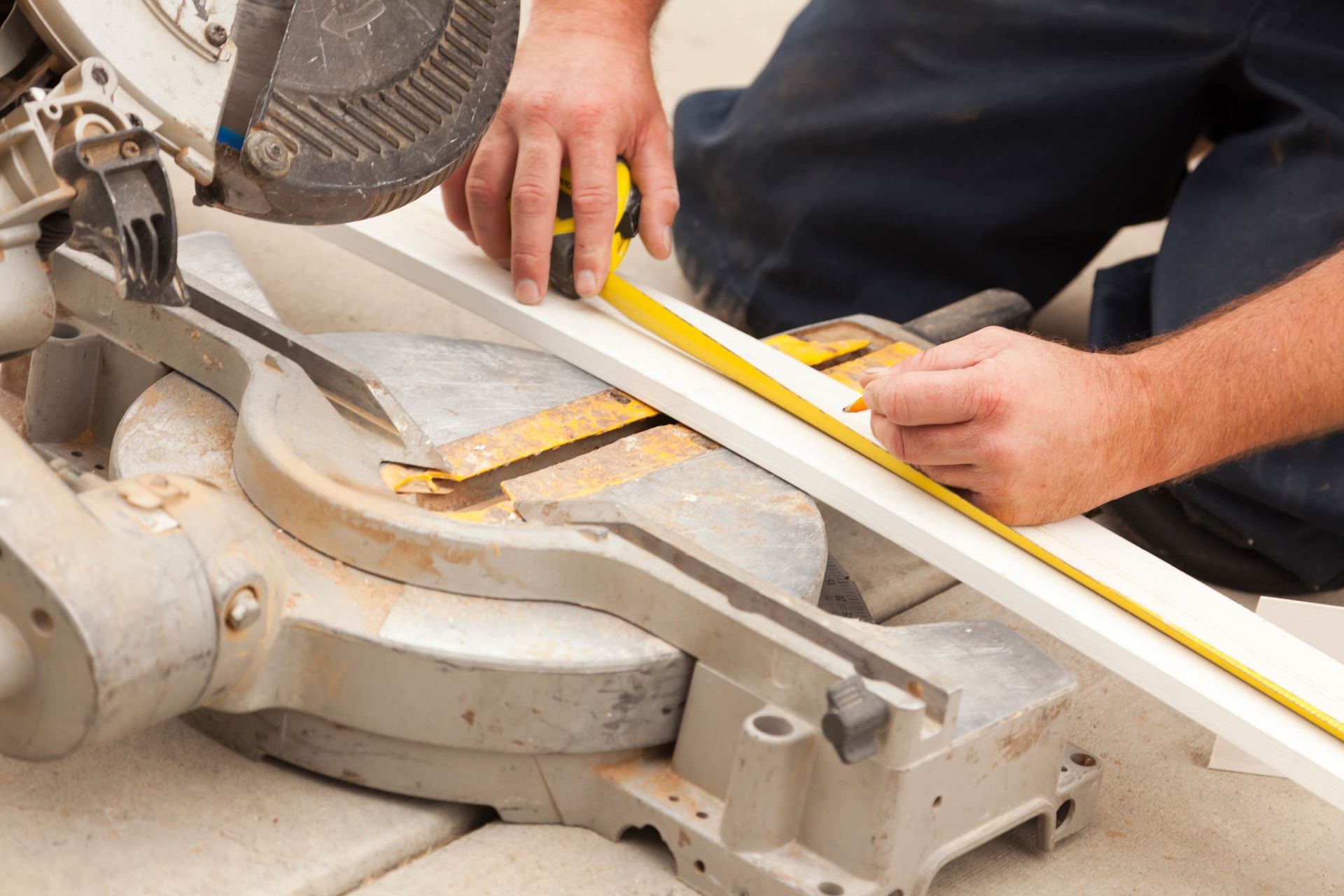 Person using a miter saw, measuring and marking a white board with a tape measure.