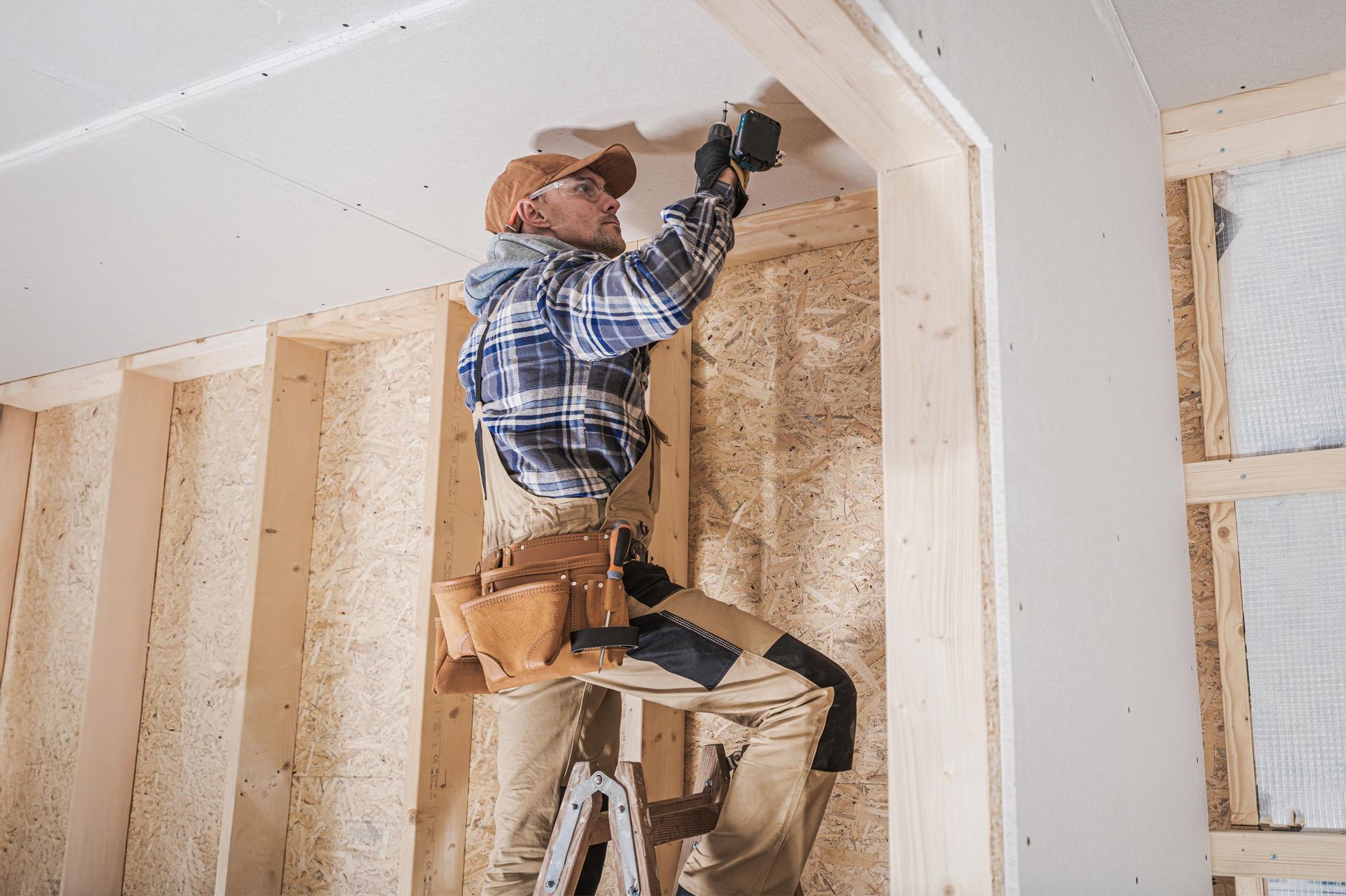 Construction worker on a ladder, installing something in a wooden frame.