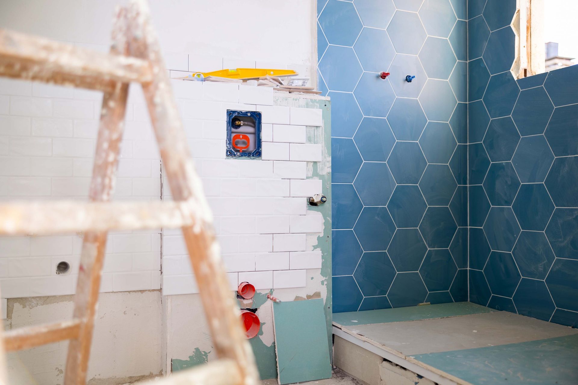Bathroom under renovation with blue hexagon tiles and a wooden ladder.