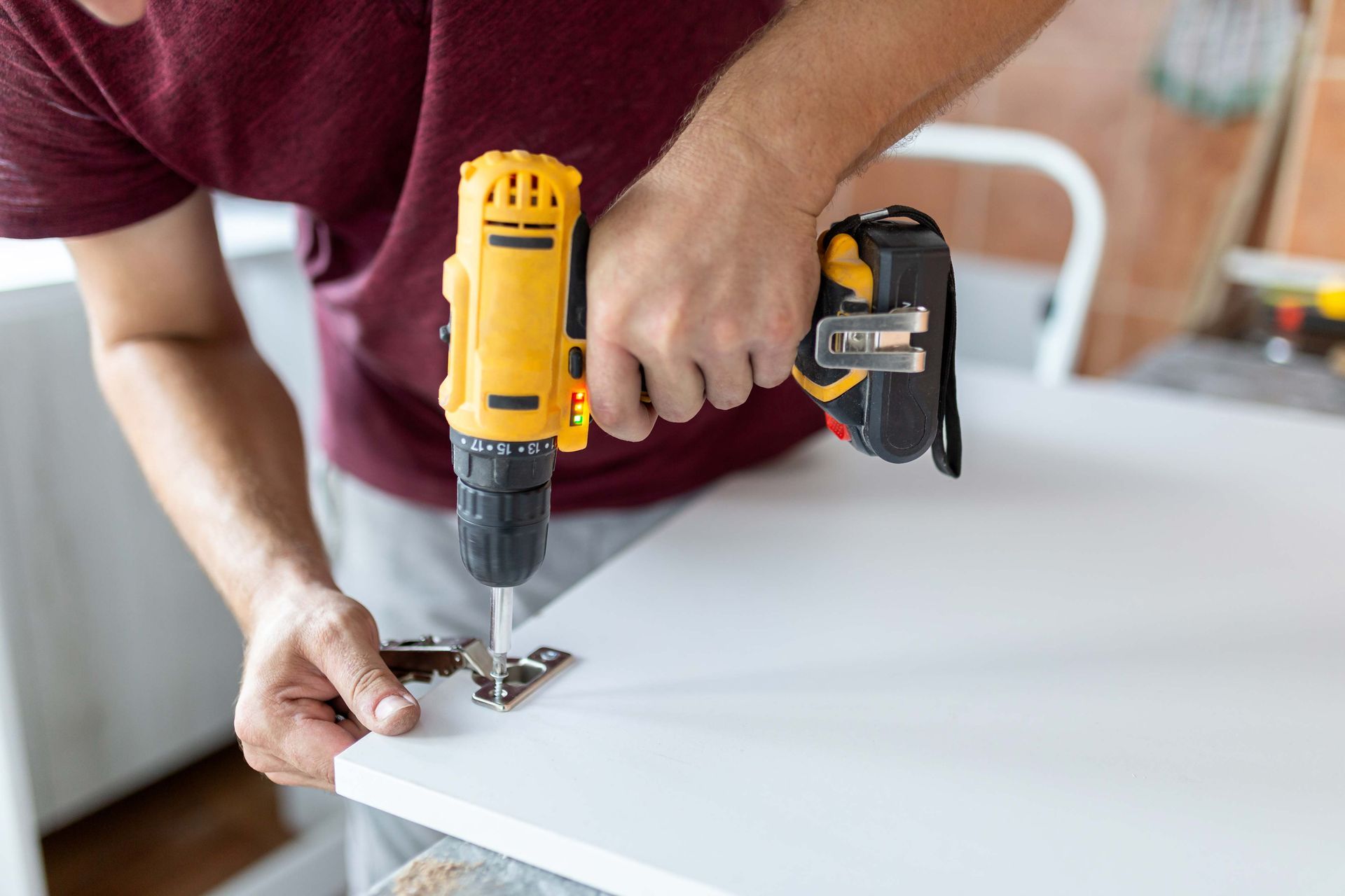 Person using a yellow drill to attach a hinge to a white surface.