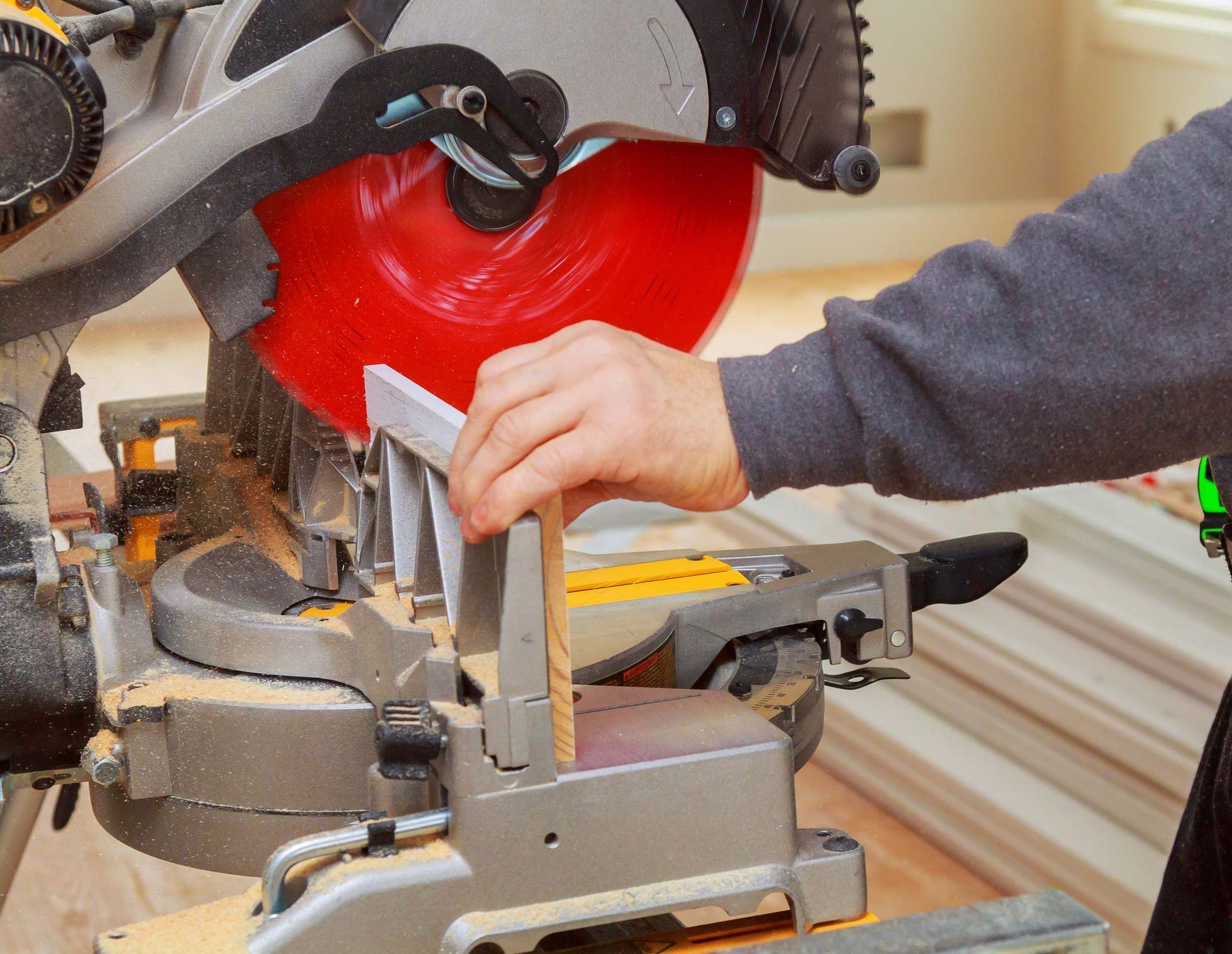 Person cutting wood with a miter saw; red blade, sawdust, and wood trim are visible.