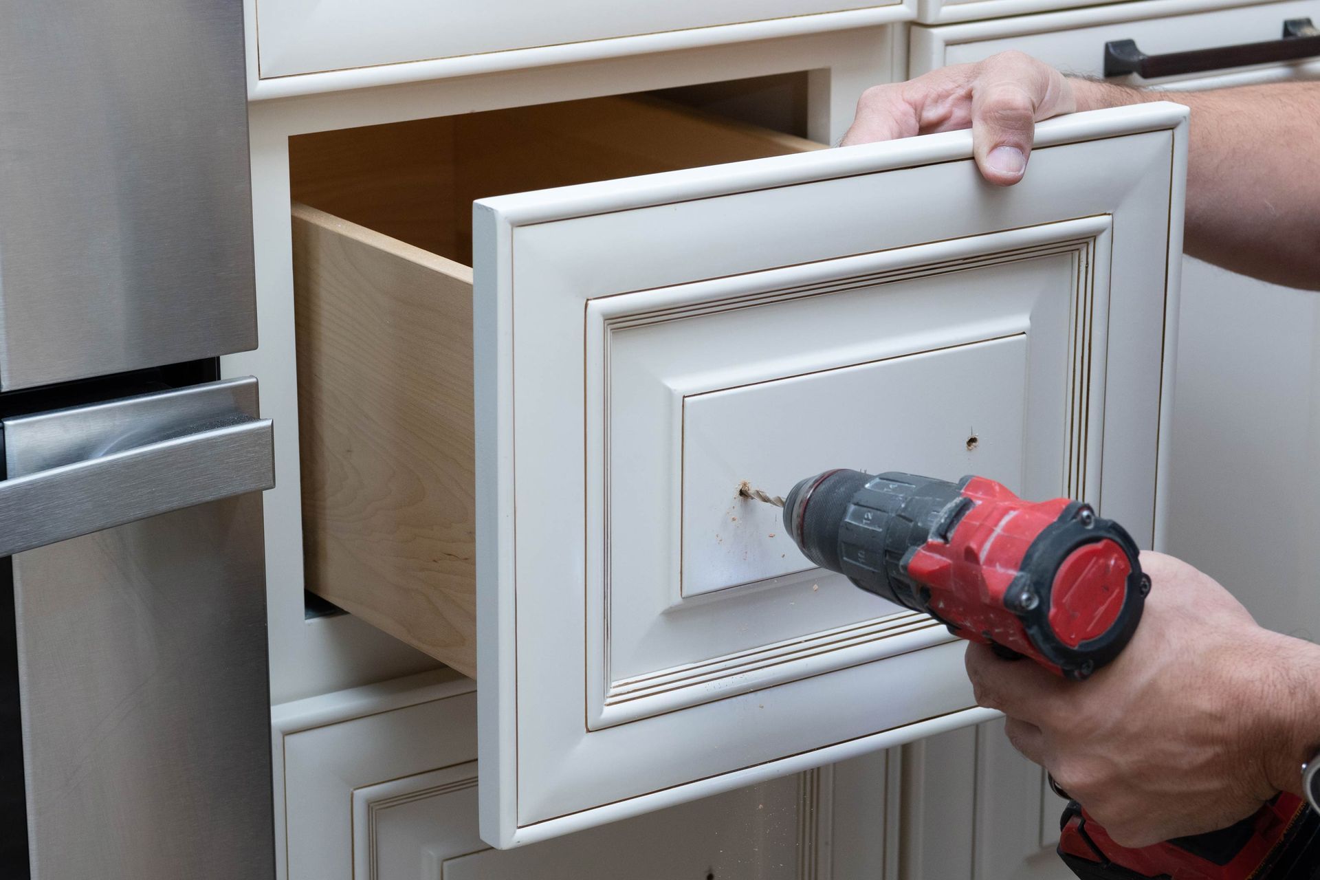 Person using a drill to install a drawer pull on a kitchen cabinet.