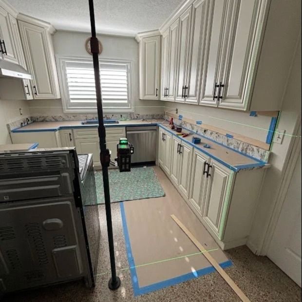 Kitchen with light cabinets, countertops, and appliances, under renovation. Green laser level in use.