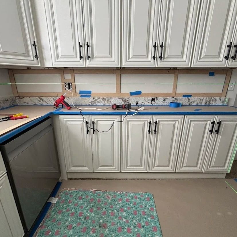 Kitchen with white cabinets, light countertops, and tools, likely in the middle of a renovation.