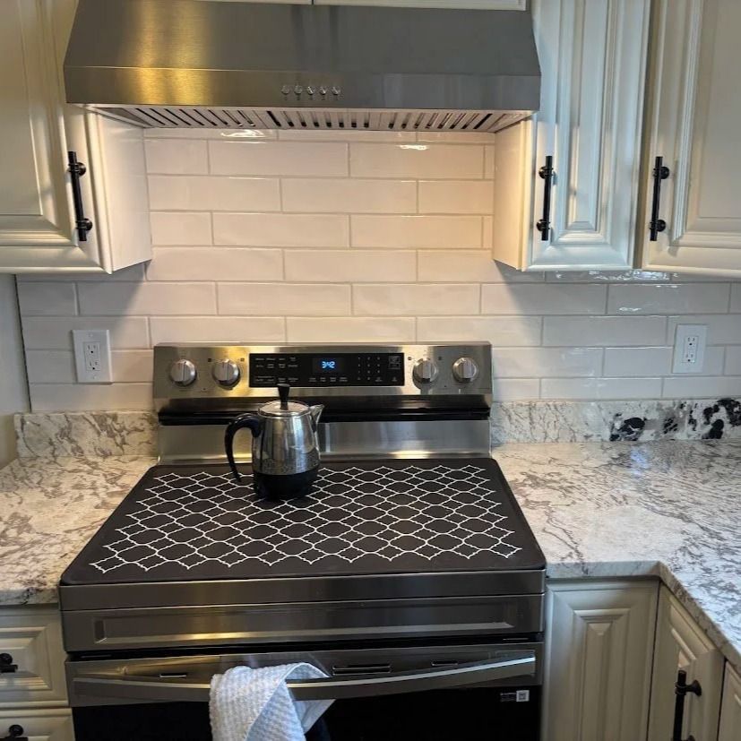 Kitchen with stainless steel stove, hood, and white cabinets, light countertops and backsplash.