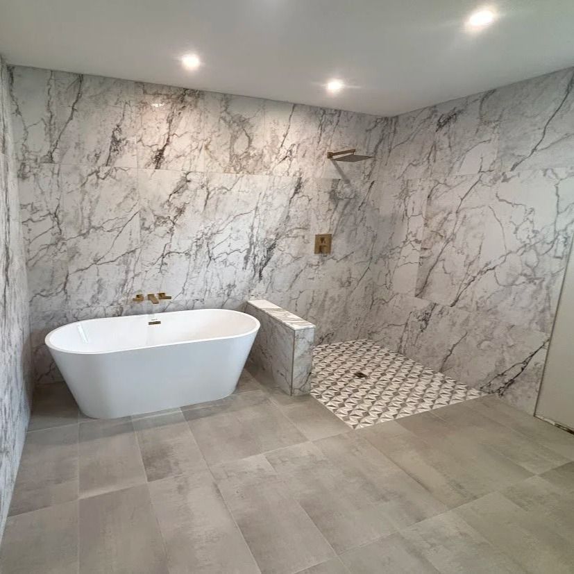 Modern bathroom with white marble-like walls and a standalone tub, tiled shower, and wood-look floors.