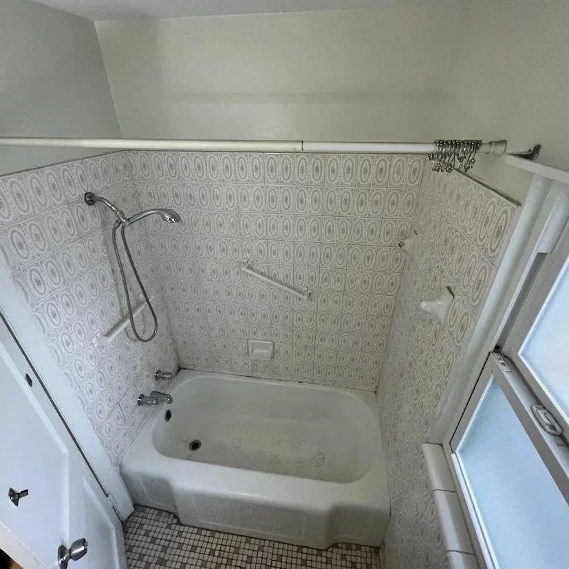 Bathroom with white tub, patterned tile, and window.