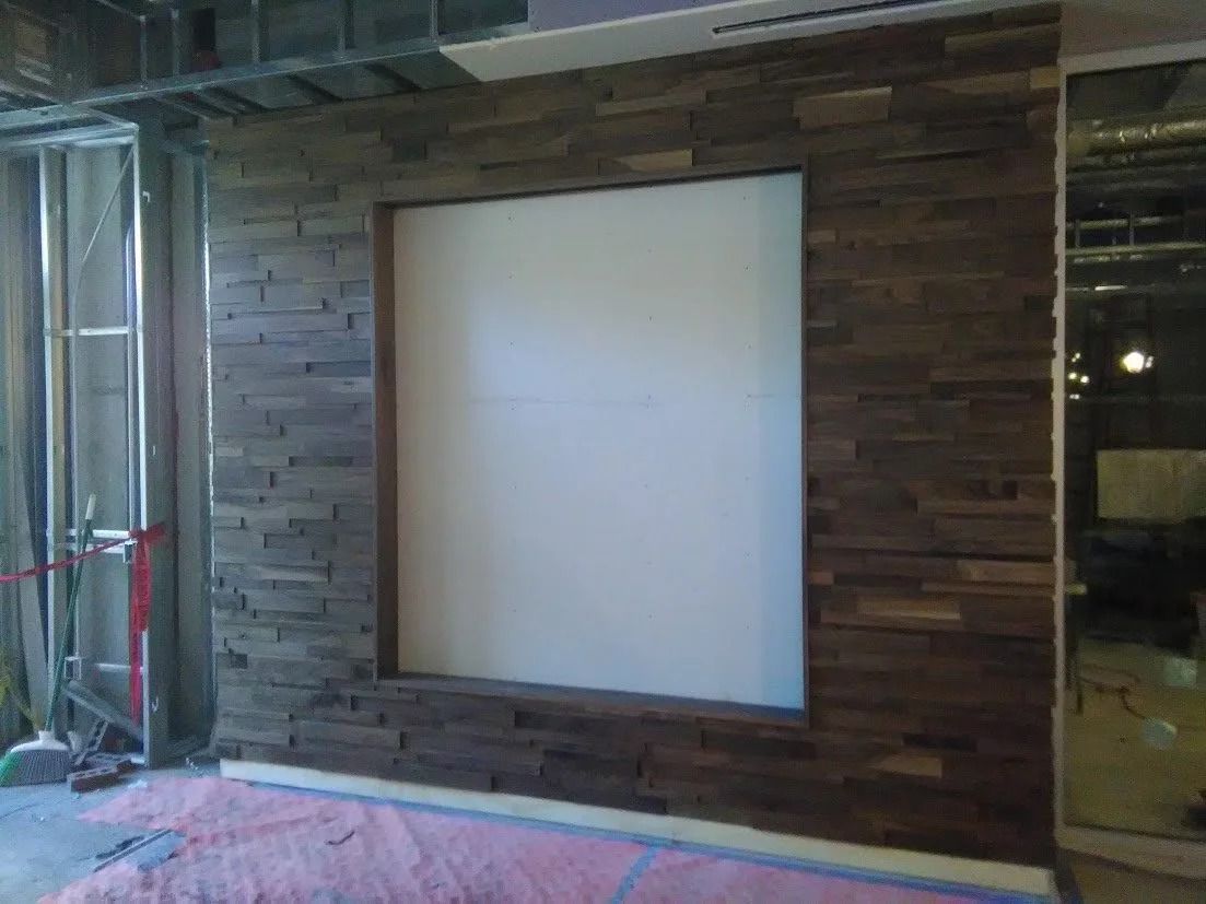 Wall with dark wood-look paneling surrounding a square, white opening; construction materials on floor.