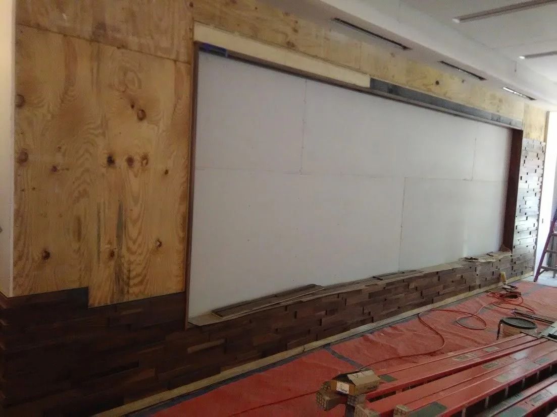 Construction in progress: plywood wall with insulation, framing, and tools on red covering.