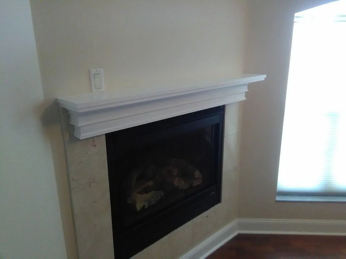 Fireplace with white mantel, set in a light-colored wall with a window in the background.