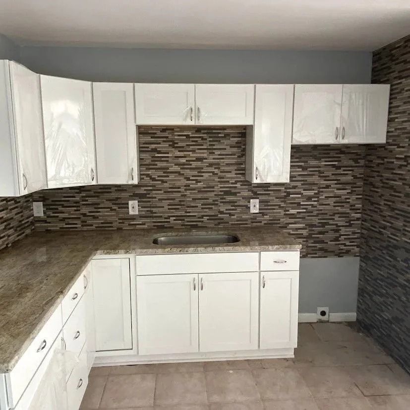 White kitchen cabinets with granite countertops against a stone tile backsplash.