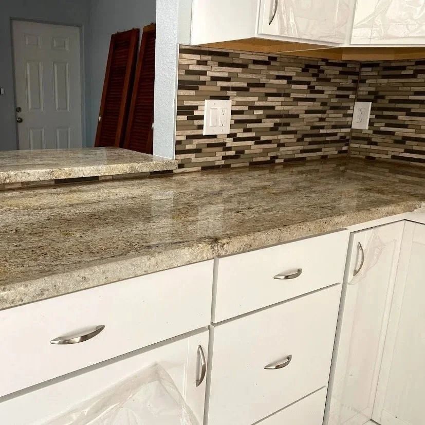White kitchen cabinets with granite countertop and mosaic tile backsplash.