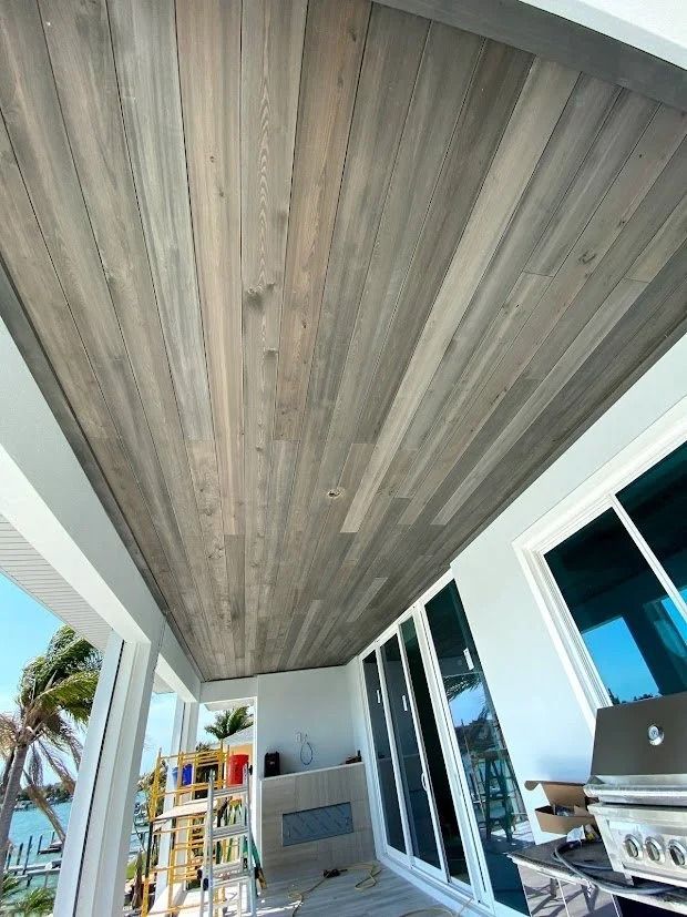 Wooden plank ceiling above a white-framed porch with sliding glass doors, overlooking a water view.