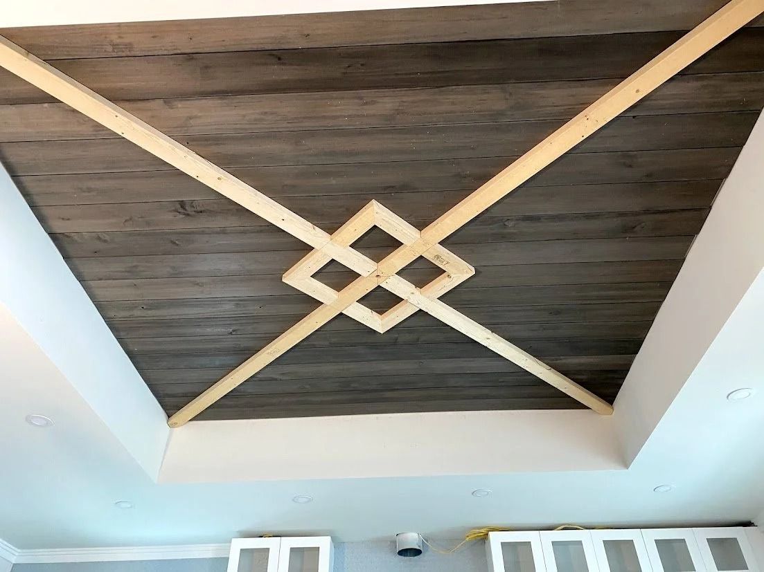 Ceiling with wooden beams in a geometric pattern, on a gray, textured surface and white walls.
