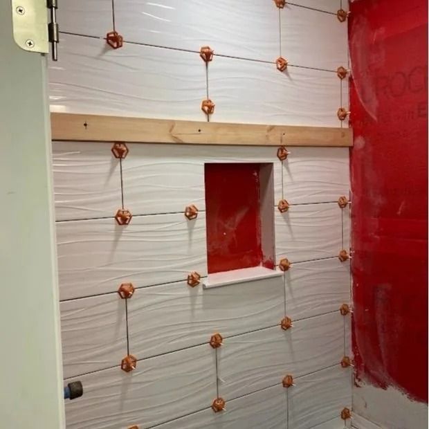 White tiled shower wall under construction with leveling spacers and niche.